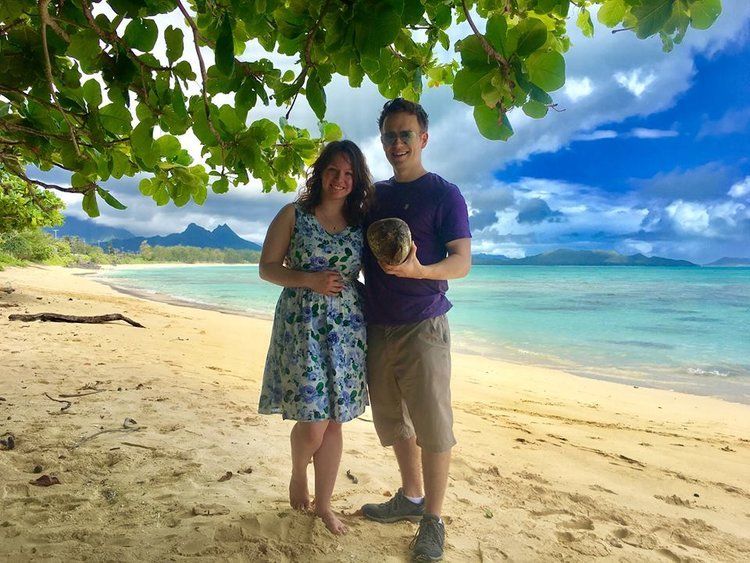 A man and a woman are standing on a beach holding a coconut.