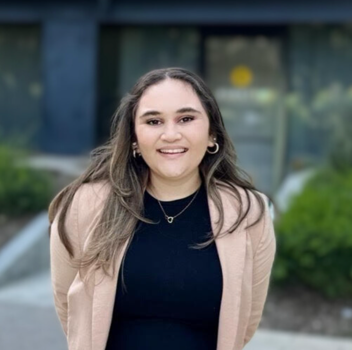 A woman wearing a black shirt and a pink jacket is smiling for the camera.