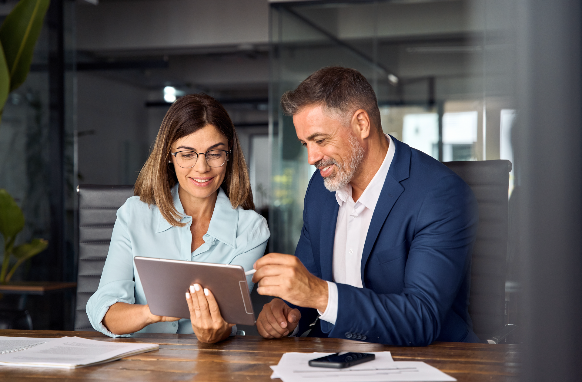 A man and a woman are sitting at a table looking at a tablet.