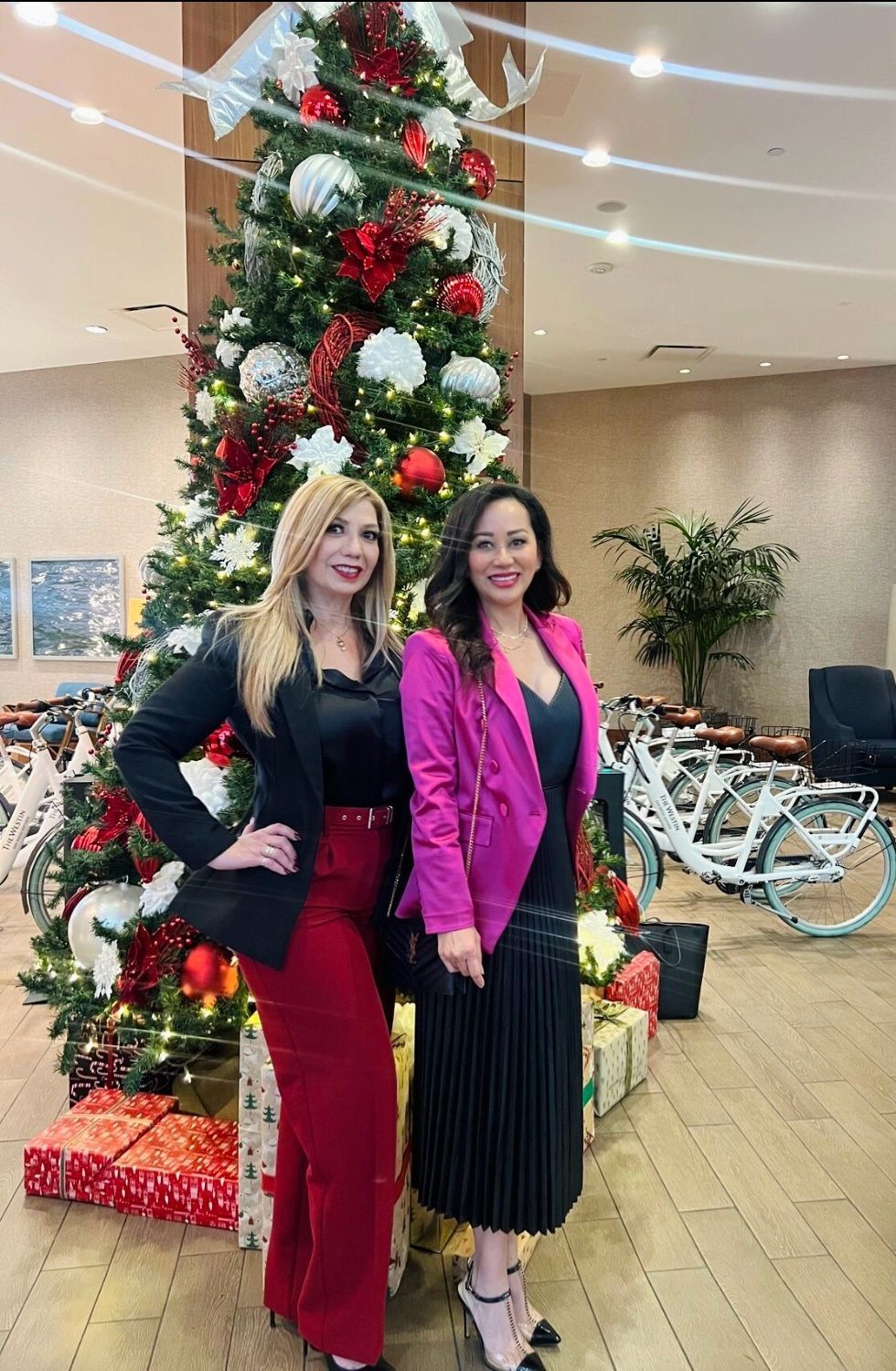 Two women are standing in front of a christmas tree.