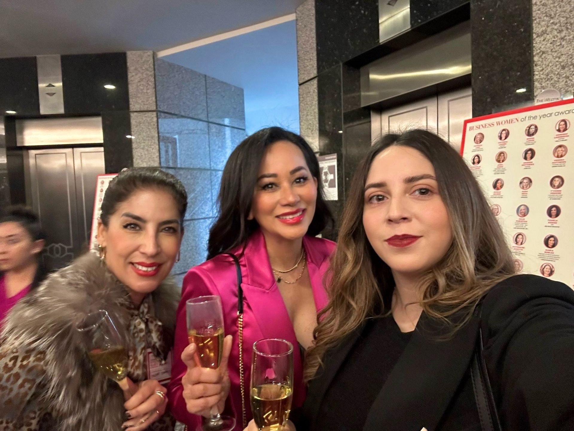 Three women are standing next to each other holding champagne glasses.