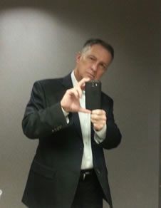 A man in a suit is taking a selfie in front of a mirror.