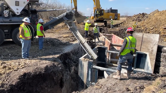 Construction workers pouring concrete from a Volumetric Mixer truck at a civil construction site .