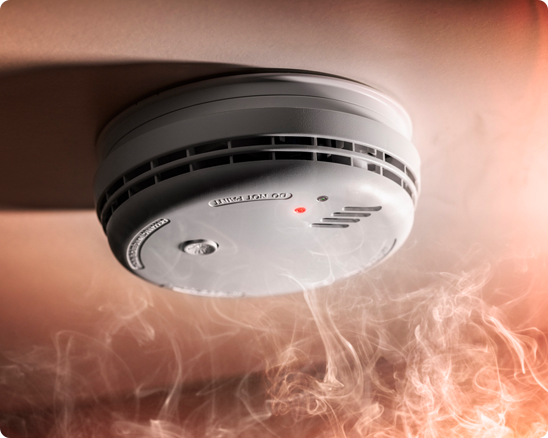 A smoke detector on a ceiling with smoke coming out of it