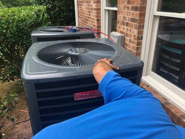An HVAC technician in uniform is servicing a home heating and cooling system.