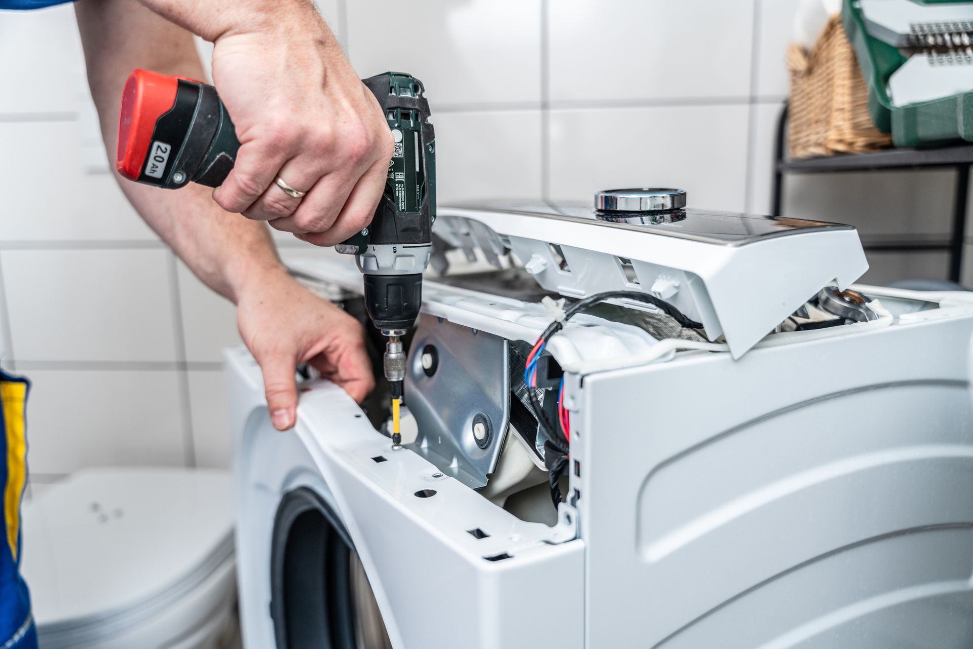 A man is fixing a washing machine with a drill.