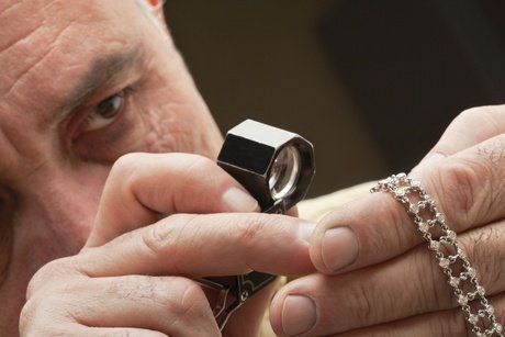 A man is looking at a necklace through a magnifying glass.