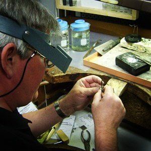 A man wearing a magnifying glass is working on a piece of metal