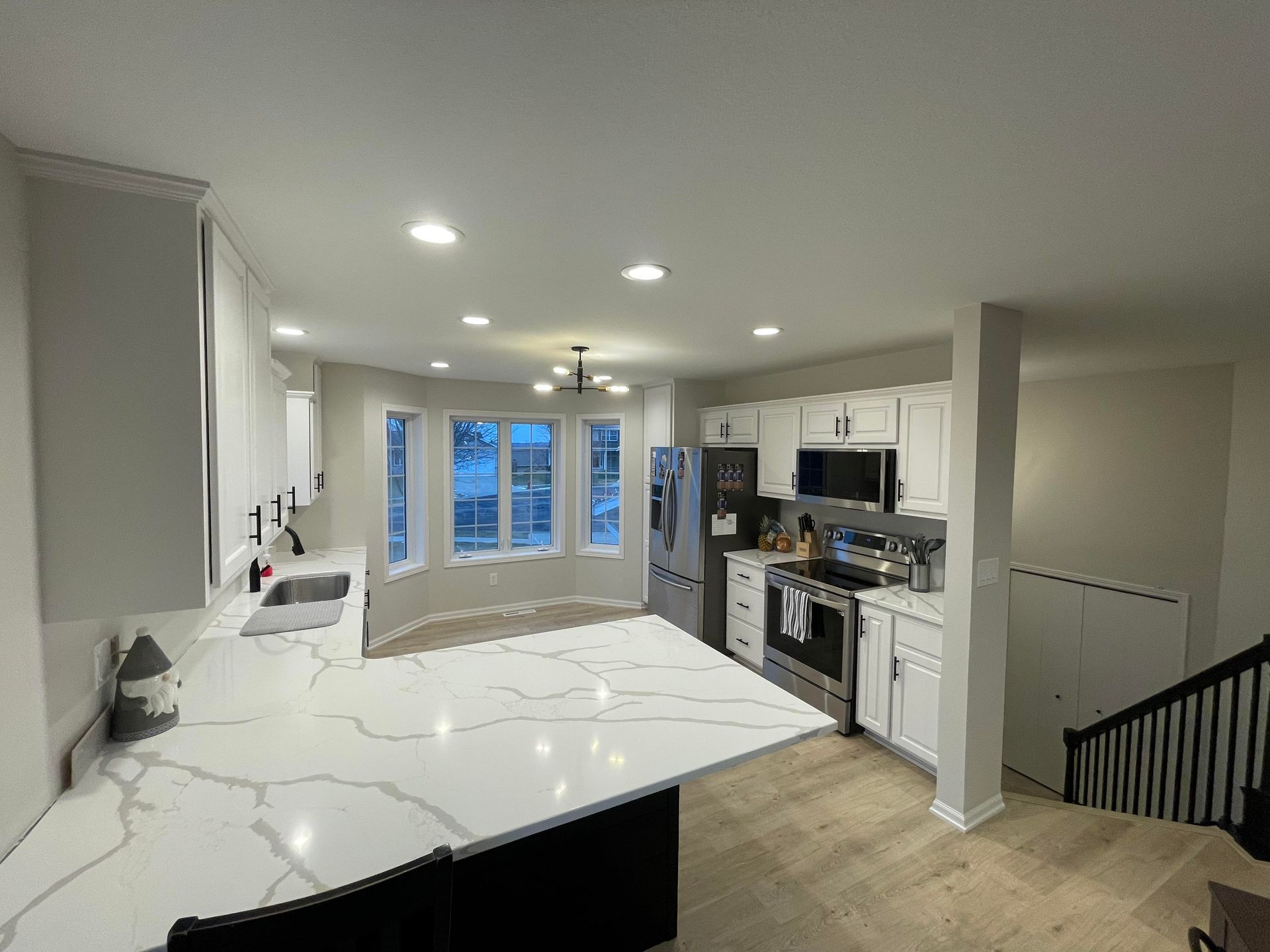 Modern white kitchen with island, stainless steel appliances, and bay window.