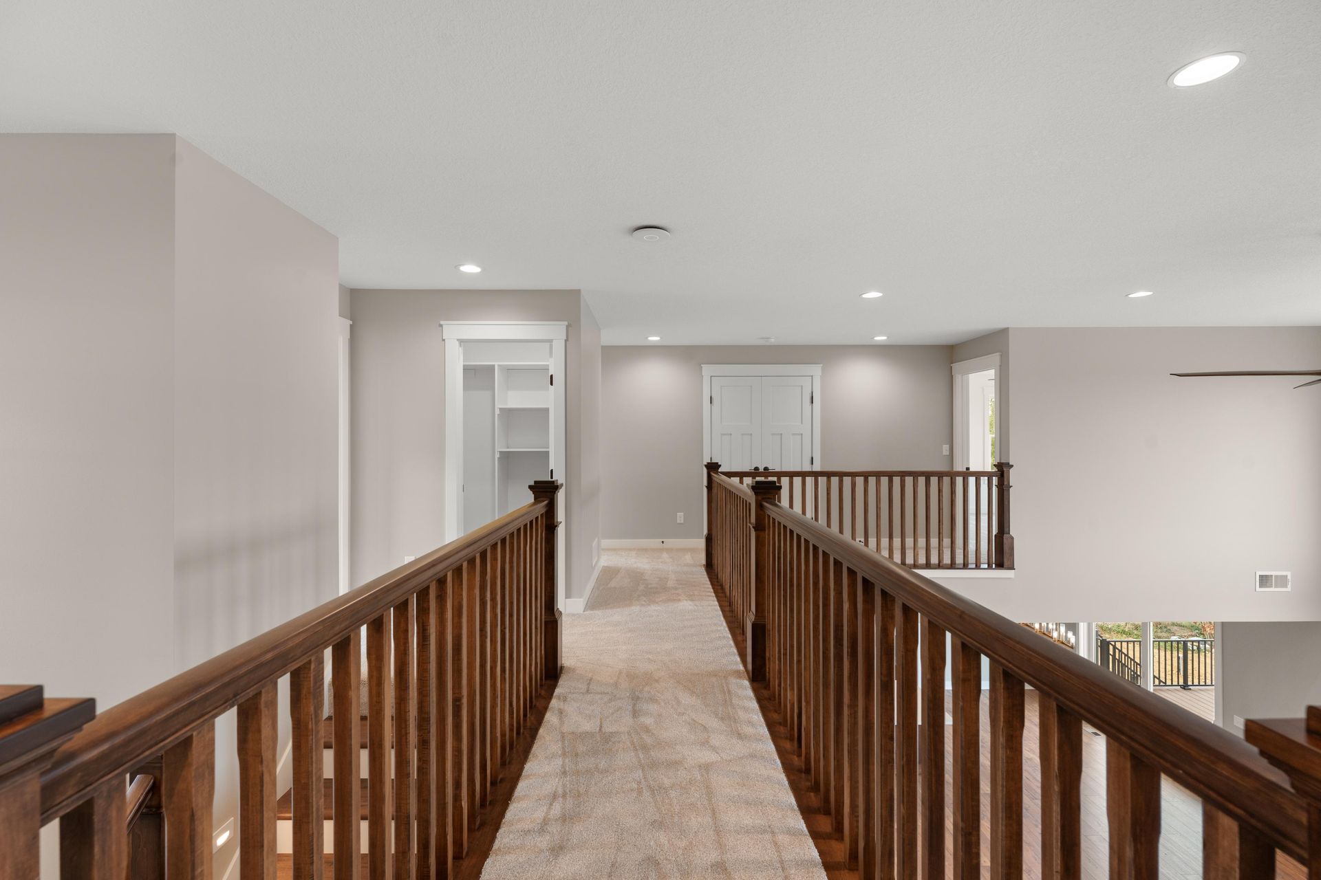 Hallway with wooden railings, carpeted floor, white doors, and recessed lighting.