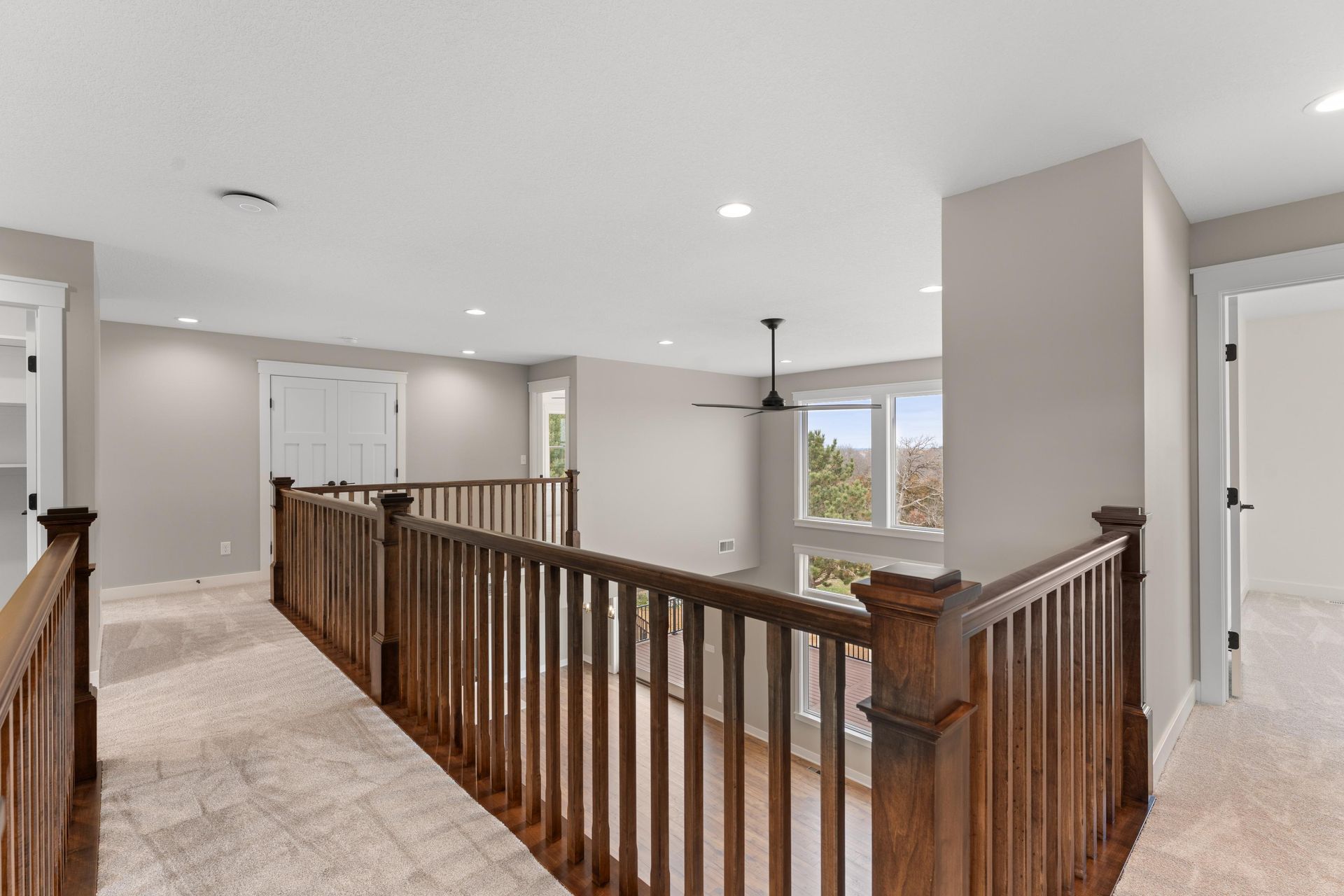Hallway with wooden railing, beige walls, and white doors. Carpeted floor.
