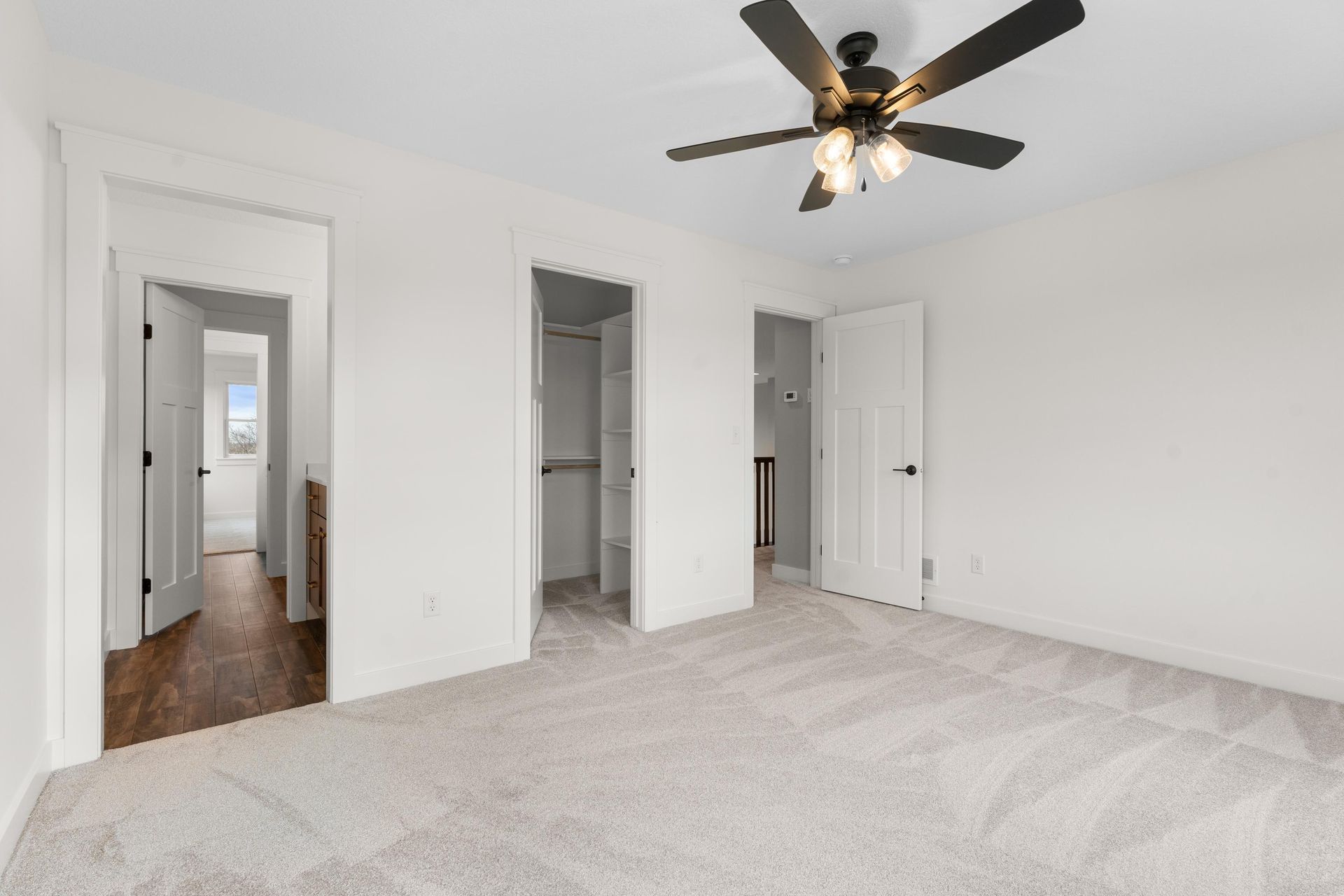 Empty bedroom with white walls, carpet, ceiling fan, and three doorways.