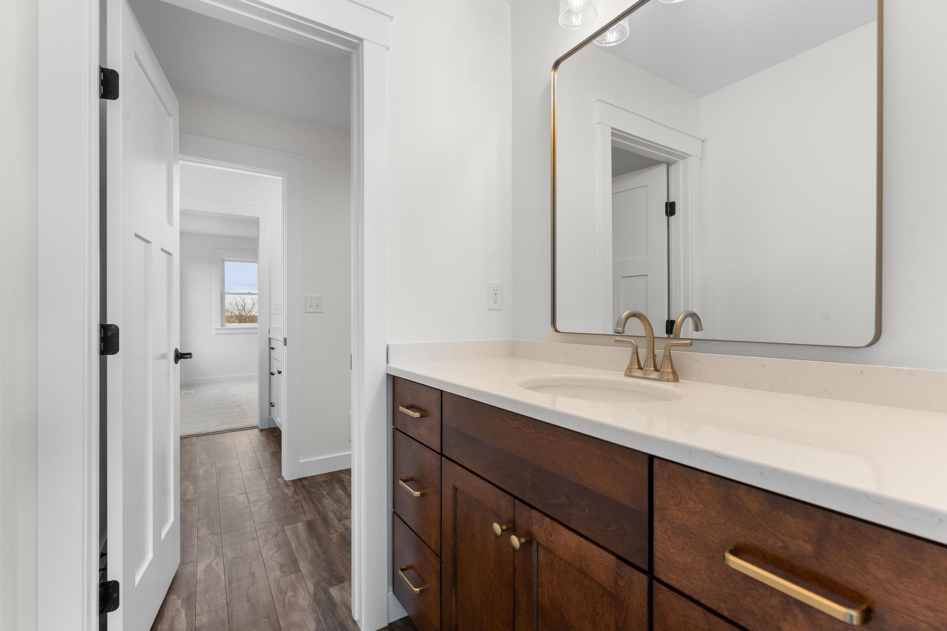 Bathroom with brown vanity, white countertop, and gold hardware. Doorway leads to hallway.