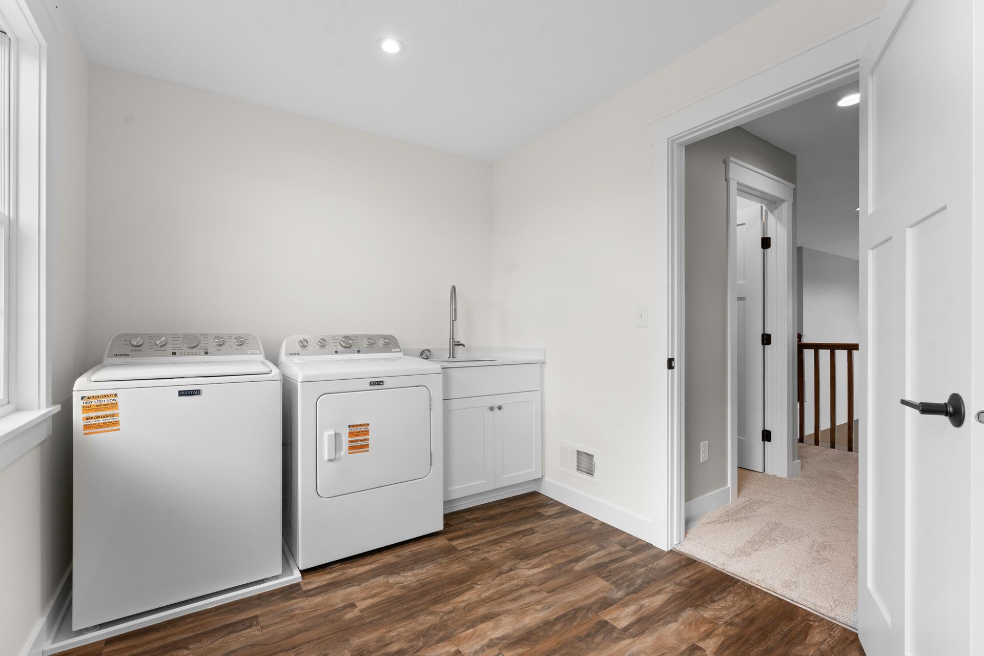 Laundry room with white appliances, wooden floor, and an open doorway.