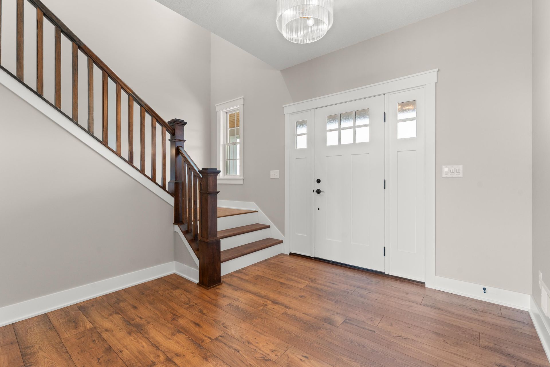 Entryway with wood flooring, white door, and stairs with dark wood railing.