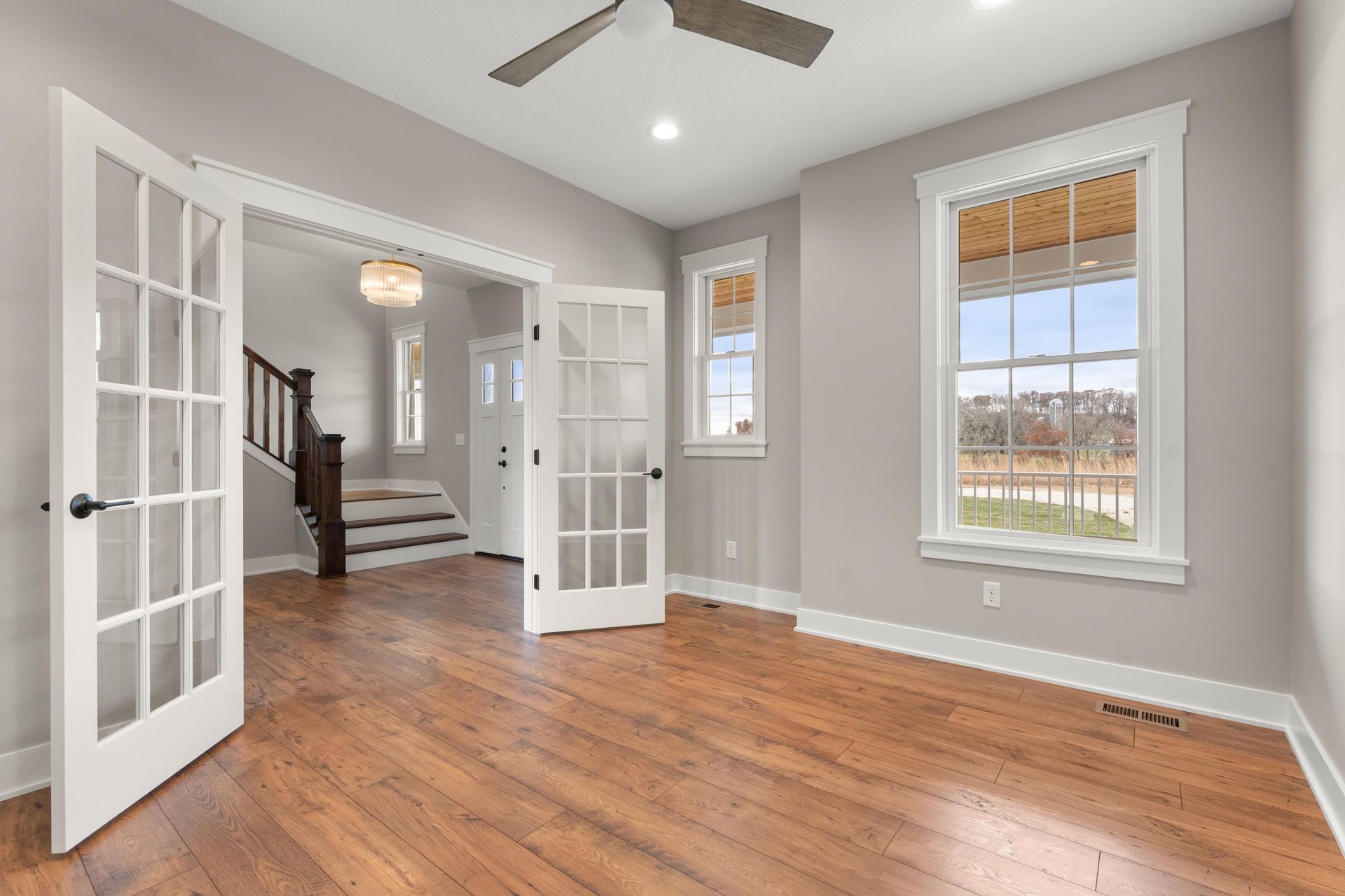 Empty room with hardwood floors, French doors, and windows, all with white trim, leading to a staircase.