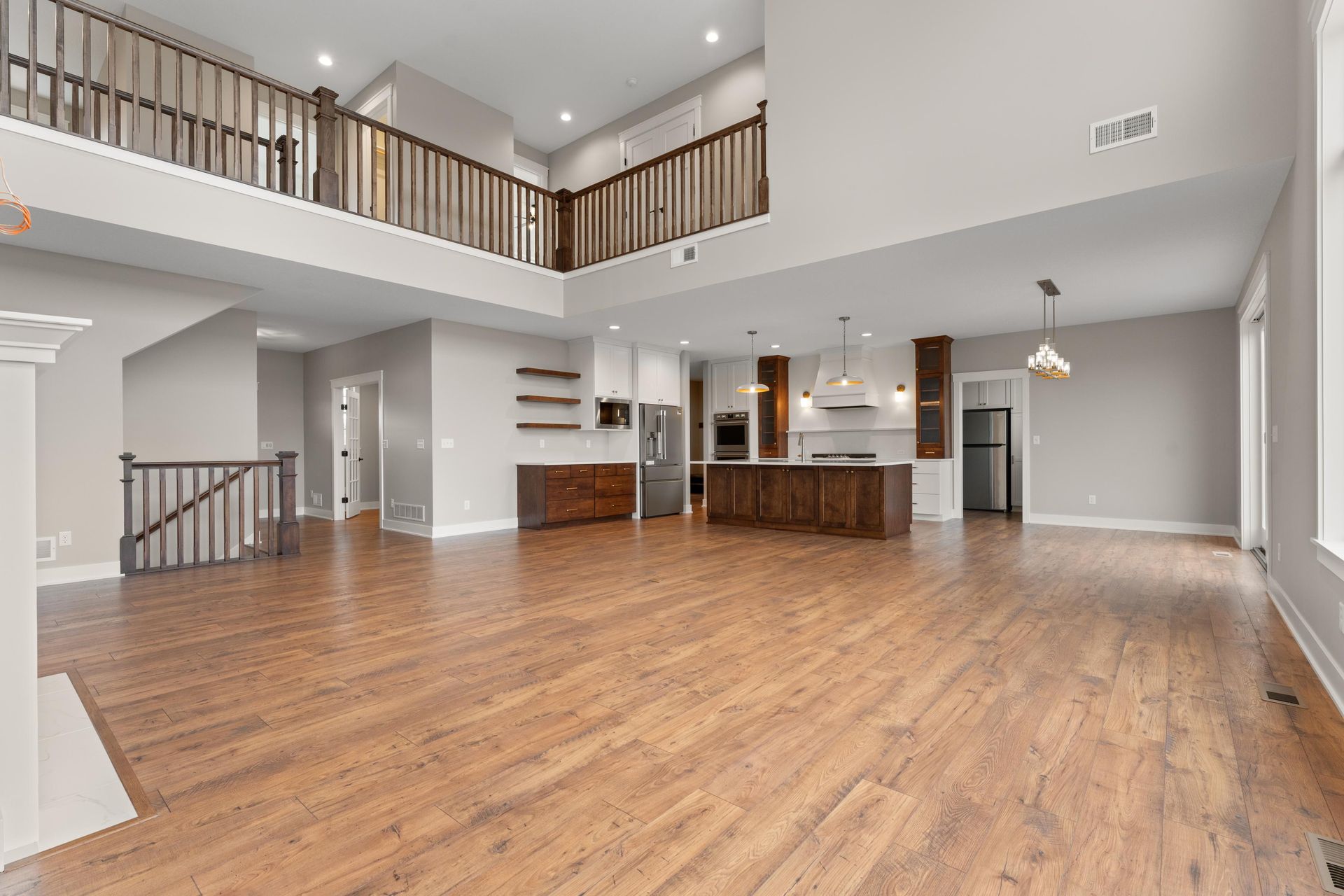 Spacious living area with wood floors, open kitchen, and loft with dark wood railings.