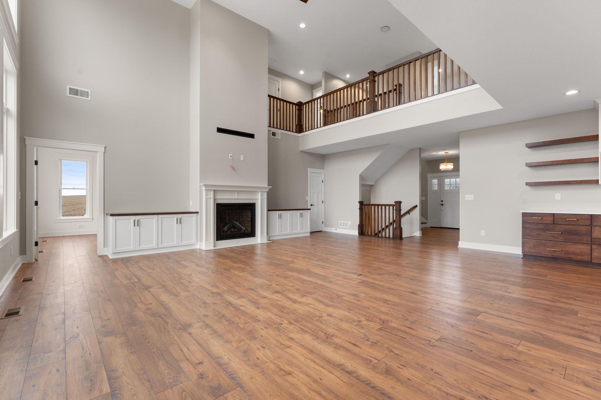Spacious living room with hardwood floors, a fireplace, and a second-story balcony.