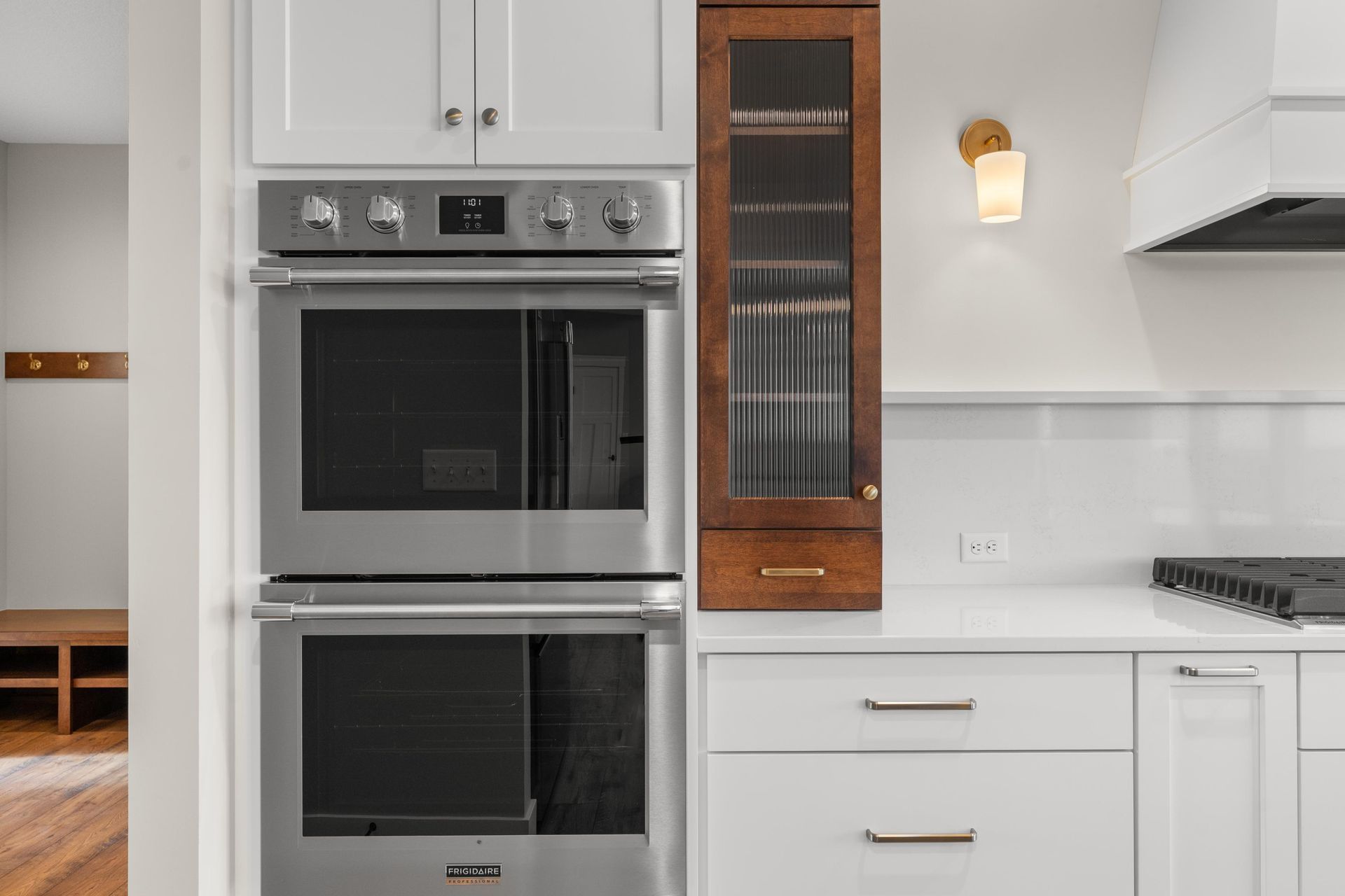 Stainless steel double oven in a white kitchen with a dark wood cabinet.