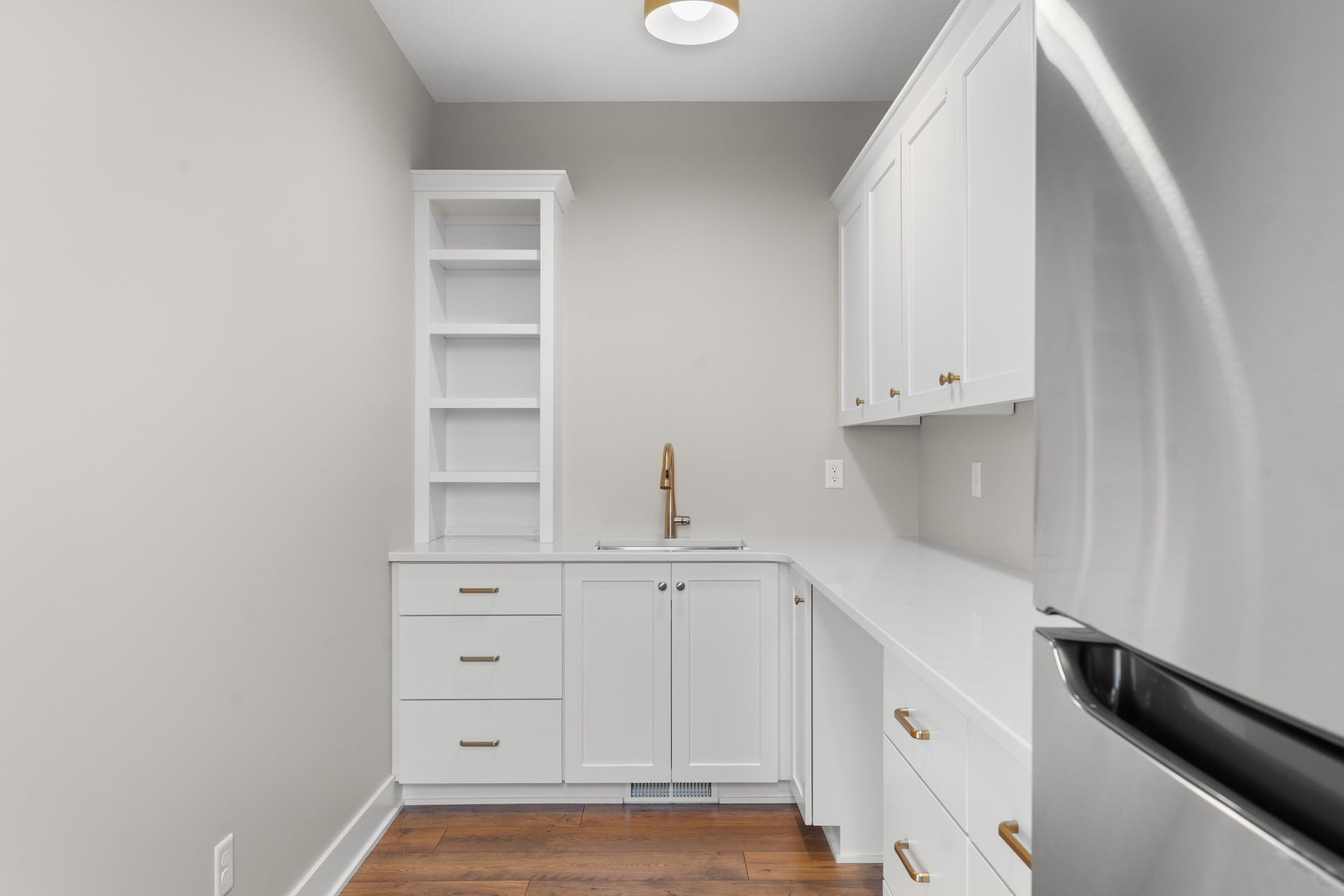 White cabinets with sink and shelving in a small kitchen area. Refrigerator to the right.