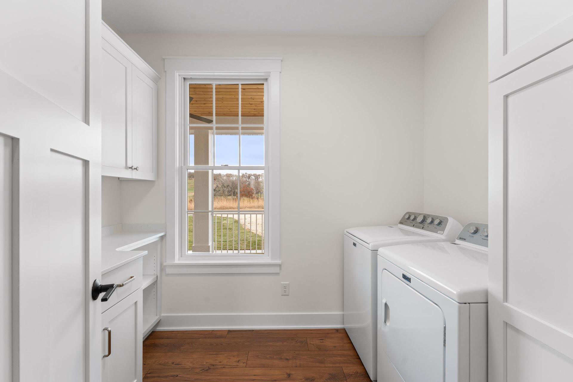 White laundry room with washer, dryer, cabinets, and a window overlooking a yard.