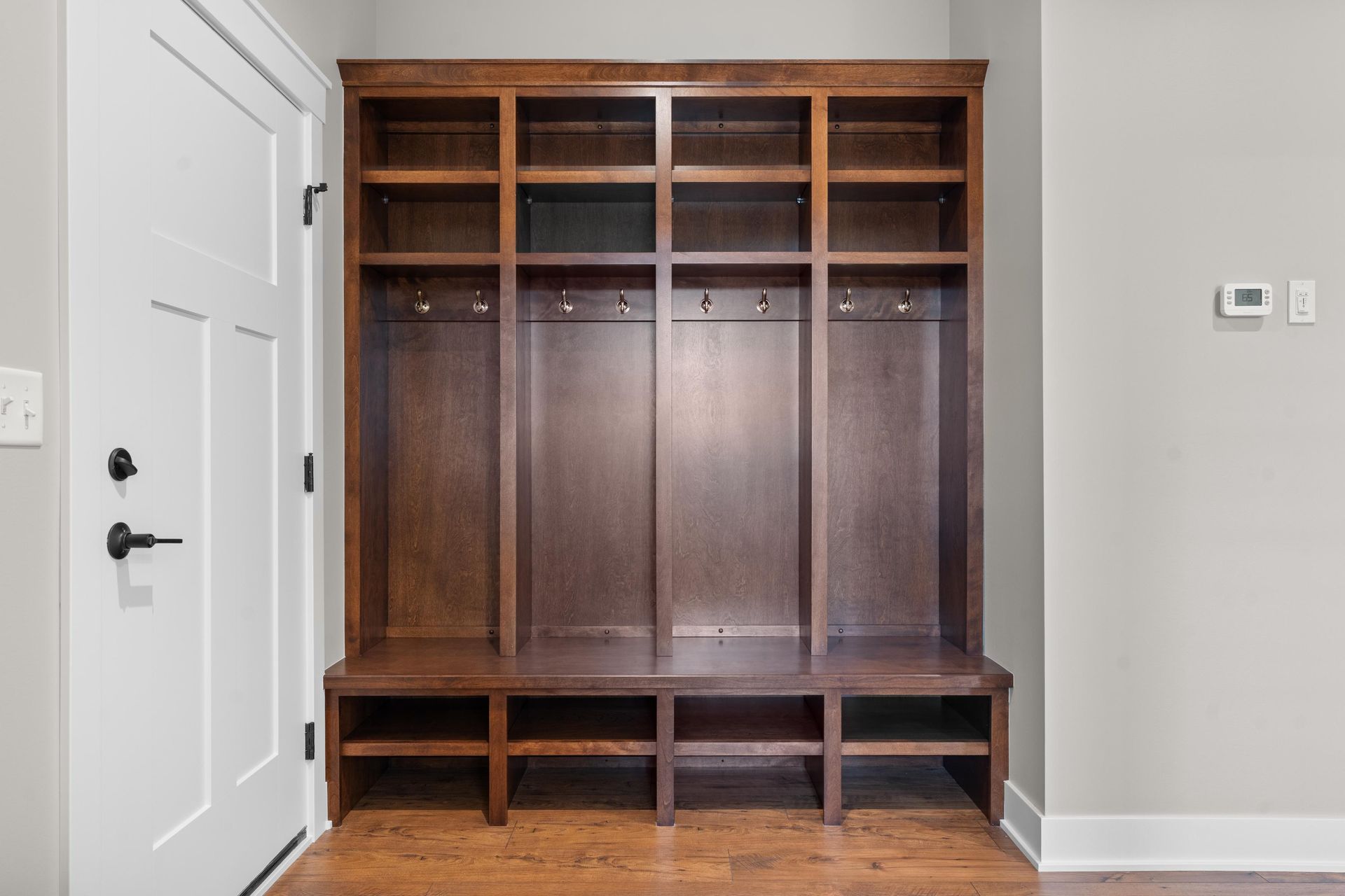 Wooden entryway organizer with shelves, hooks, and shoe storage, next to a white door.