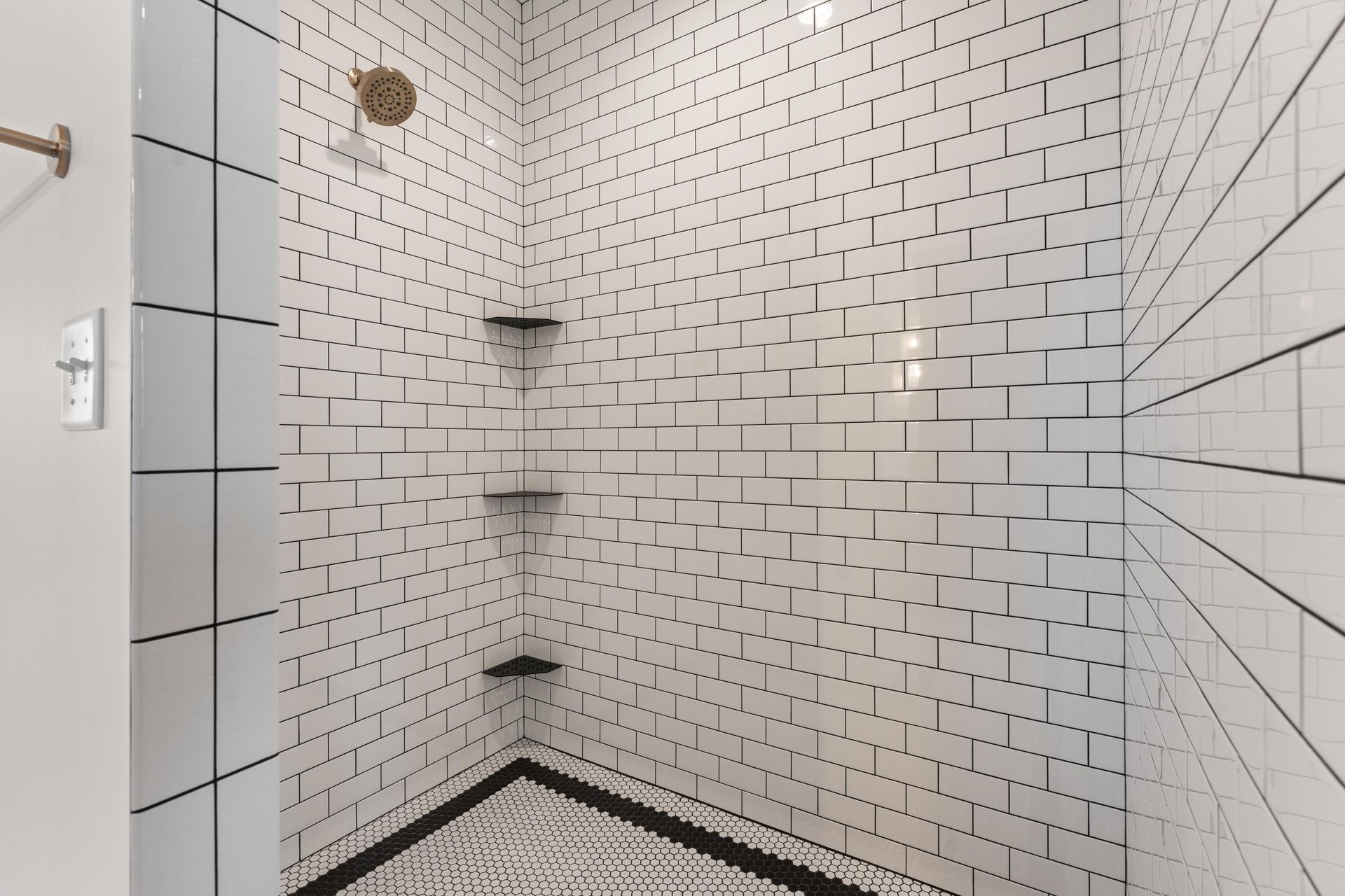 White subway tile shower with black grout and shelves. Black and white patterned floor.