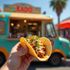 Hand holding a taco in front of a turquoise food truck with 