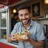 Man in front of food truck smiles, holding a sandwich.