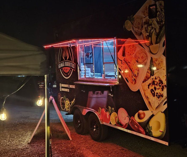 Food truck at night, lit with red lights, decorated with food images, and string lights on a nearby tent.