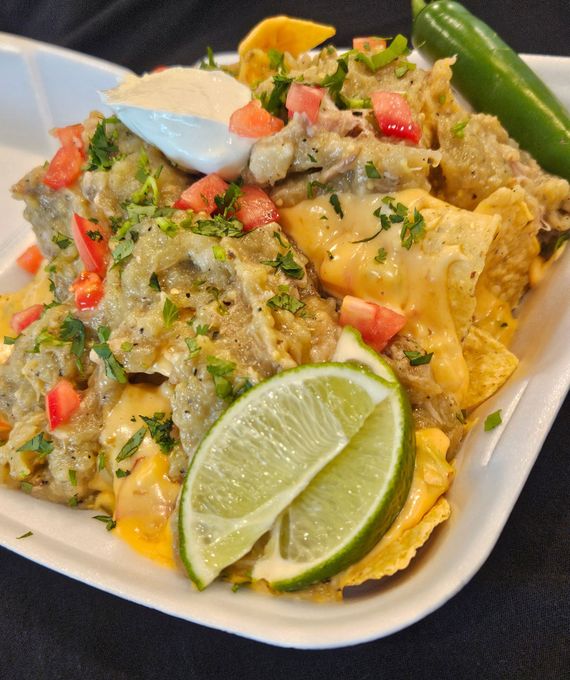 Tacos on a wooden board: Corn tortillas filled with meat, tomatoes, cilantro, and cheese, with lime slices.