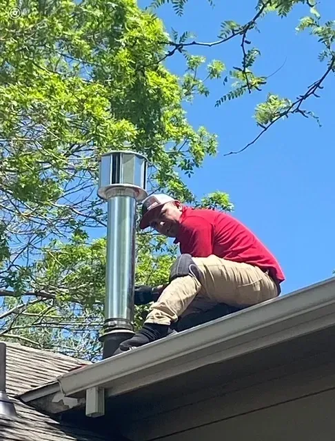 A man is sitting on the roof of a house working on a chimney