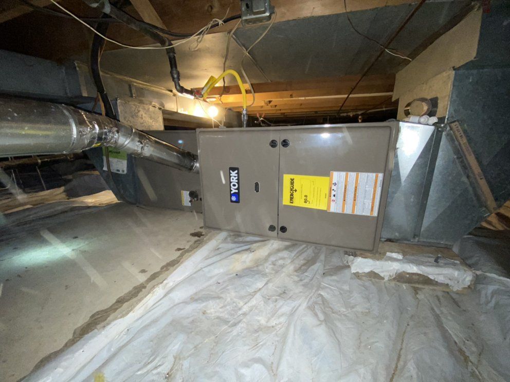 A furnace is sitting in the ceiling of a basement.
