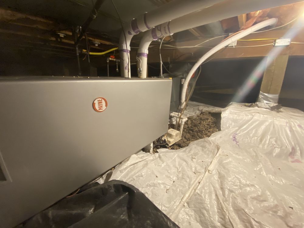 An air conditioner is sitting under a ceiling in a basement.