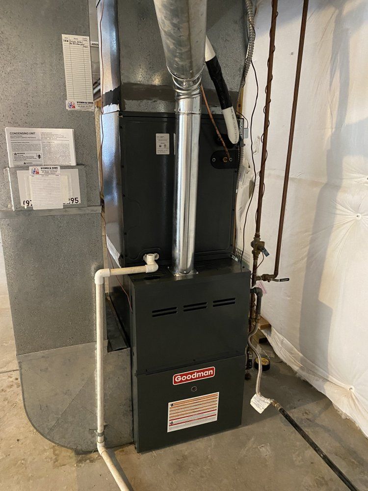 A black furnace is sitting in a basement next to a wall.