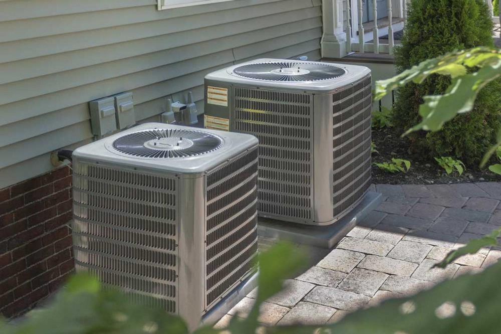 Two air conditioners are sitting on the side of a house.
