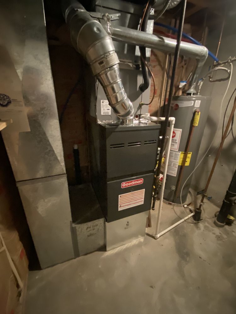 A furnace is sitting in a basement next to a water heater.