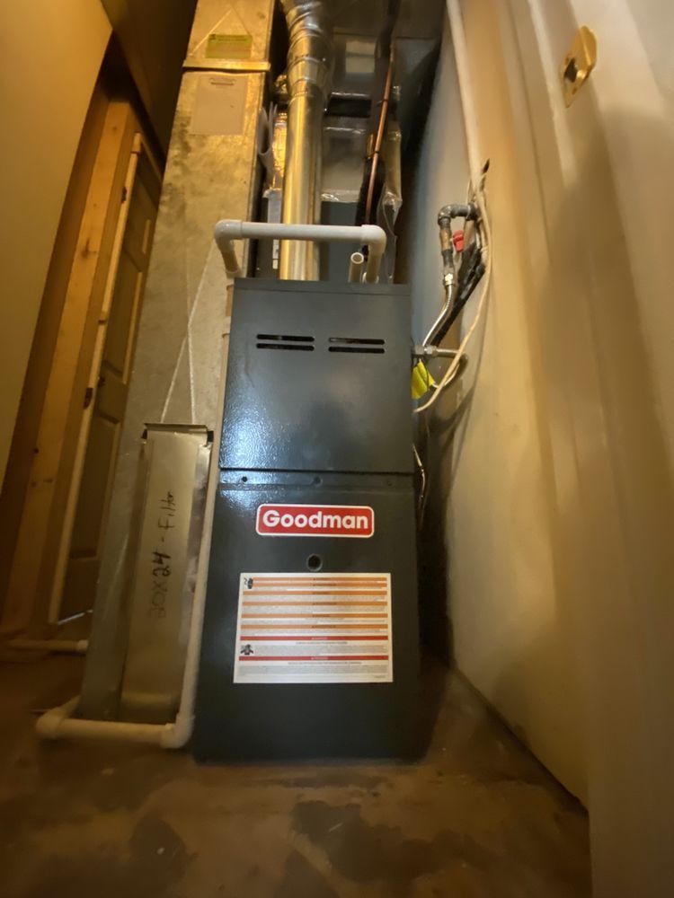 A goodman furnace is sitting in a narrow hallway next to a door.
