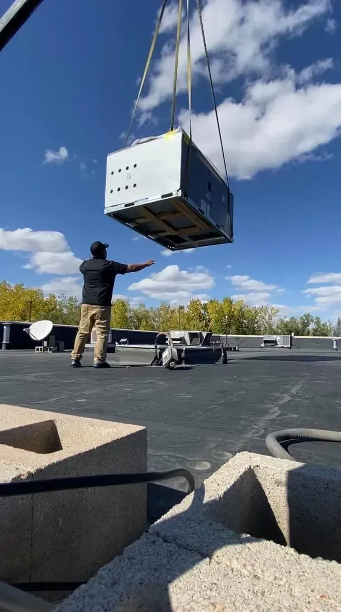 A man is standing on a roof next to a crane lifting a large box.