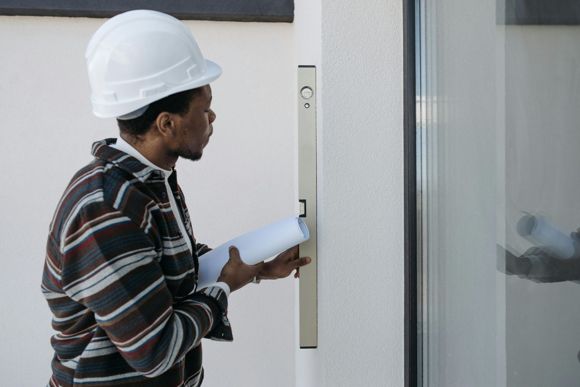 A man wearing a hard hat is holding a blueprint and a level.