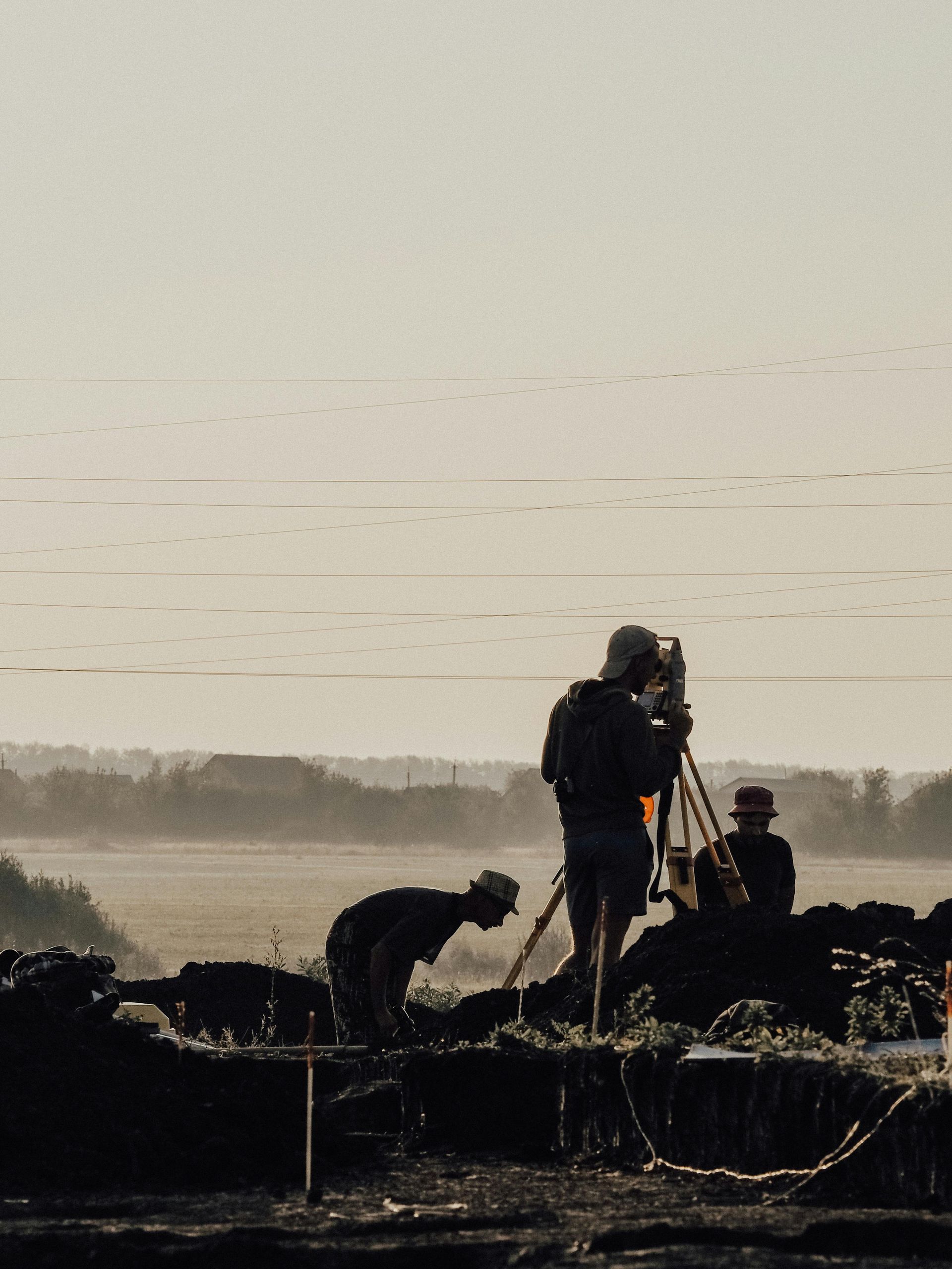 A group of men are working in a field and one is using a tripod to take a picture