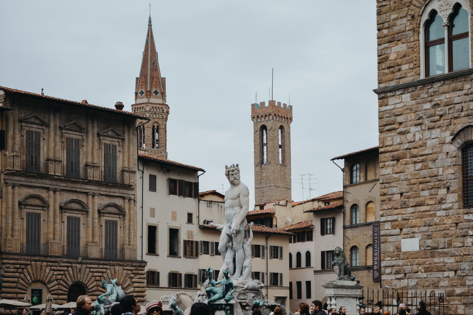 A group of people are standing in front of a statue in a city square.