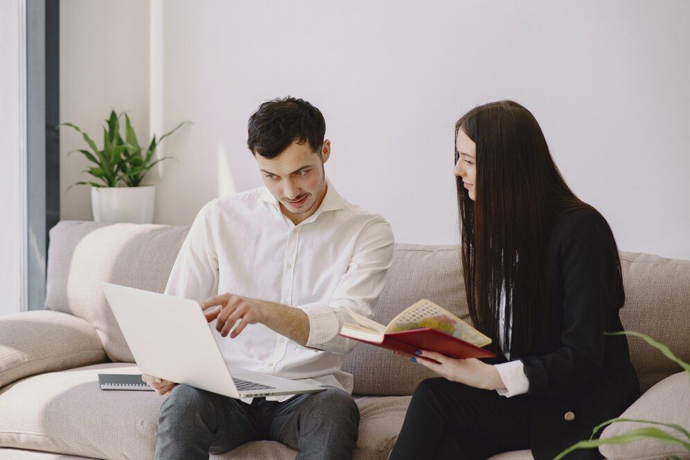 A man and a woman are sitting on a couch looking at a laptop.