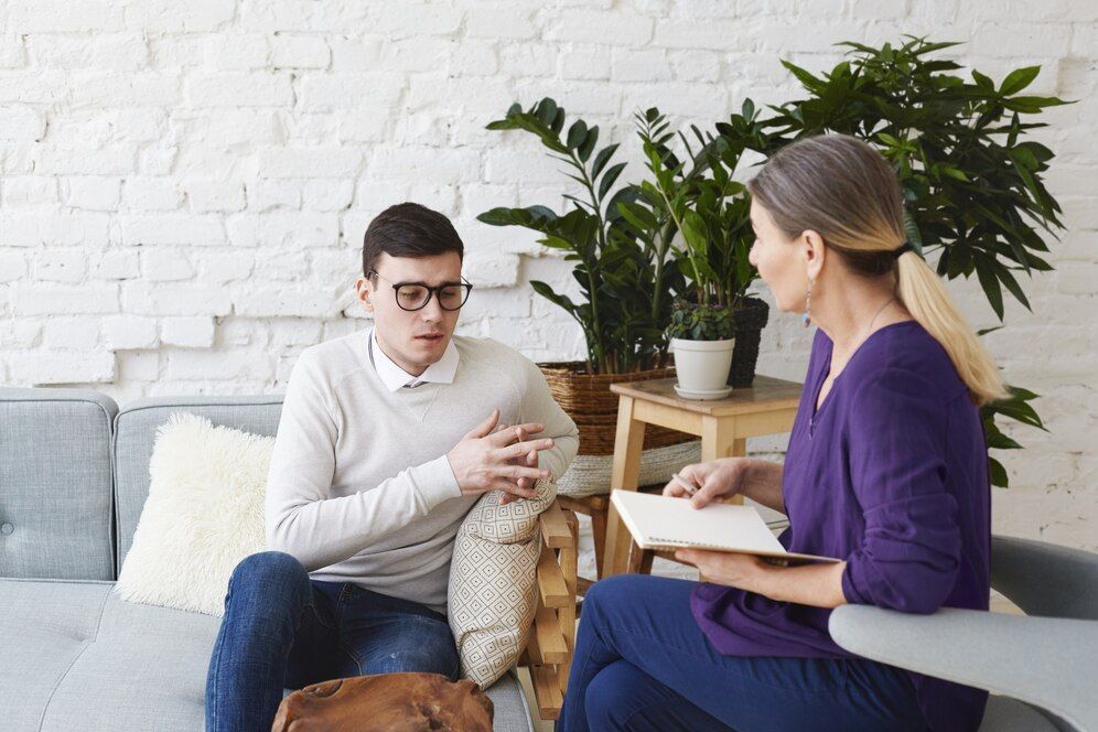 A man and a woman are sitting on a couch talking to each other.