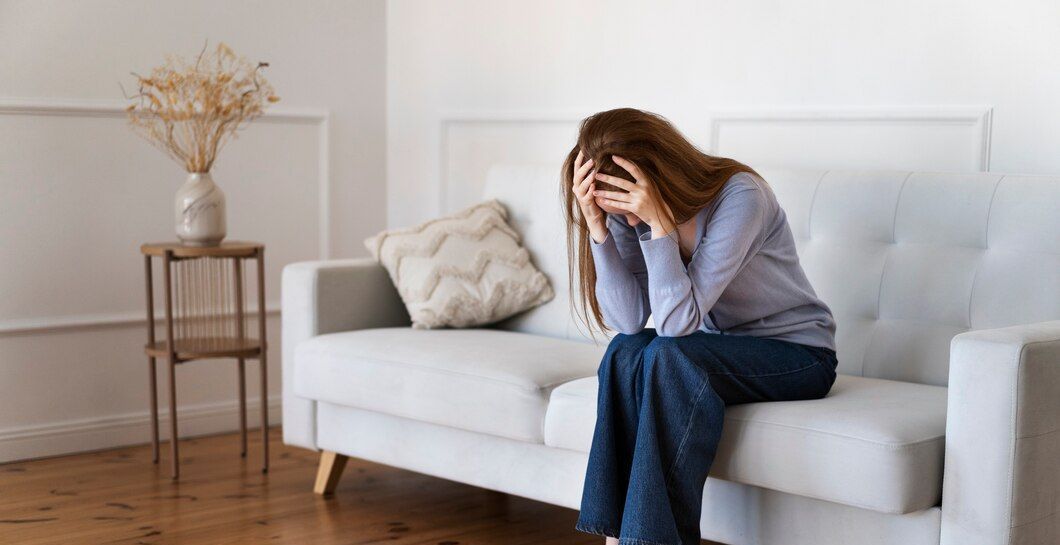 A woman is sitting on a couch with her head in her hands.