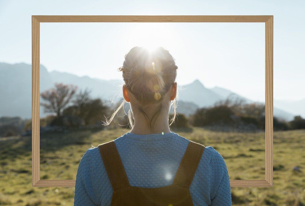 A woman with a backpack is looking at the sun through a wooden frame.