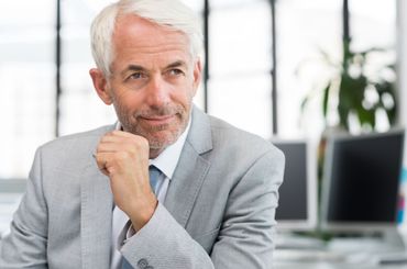 A man in a suit and tie is sitting at a desk with his hand on his chin.