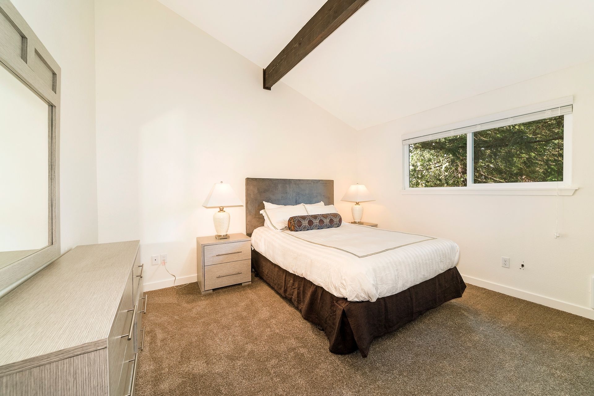 A bedroom with a bed , nightstand , mirror and window.