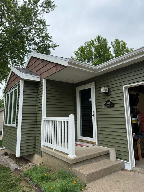 Small house porch with green siding, white railing, and an open front door under a cloudy sky.