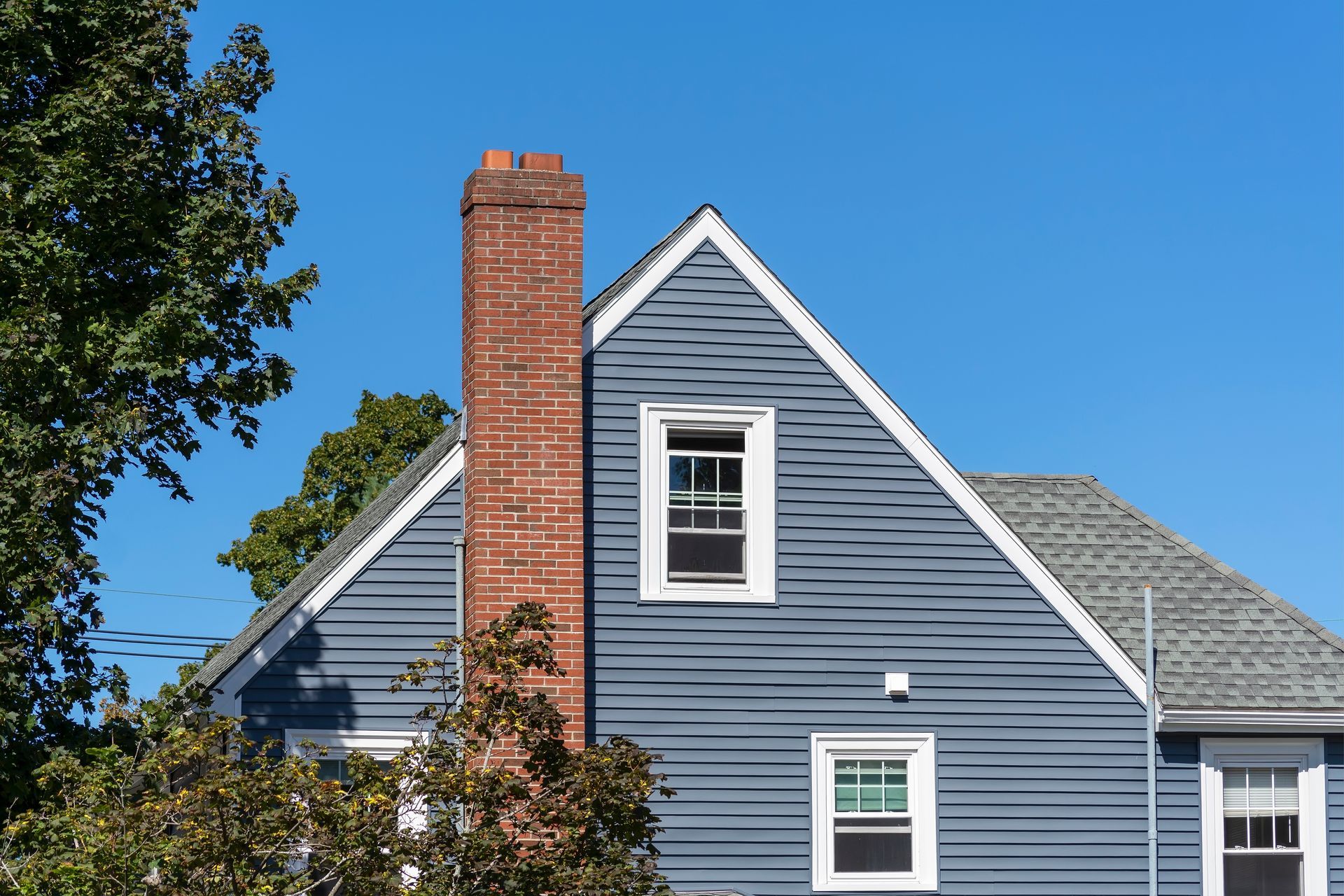 Blue house with white trim and a tall red brick chimney against a clear blue sky